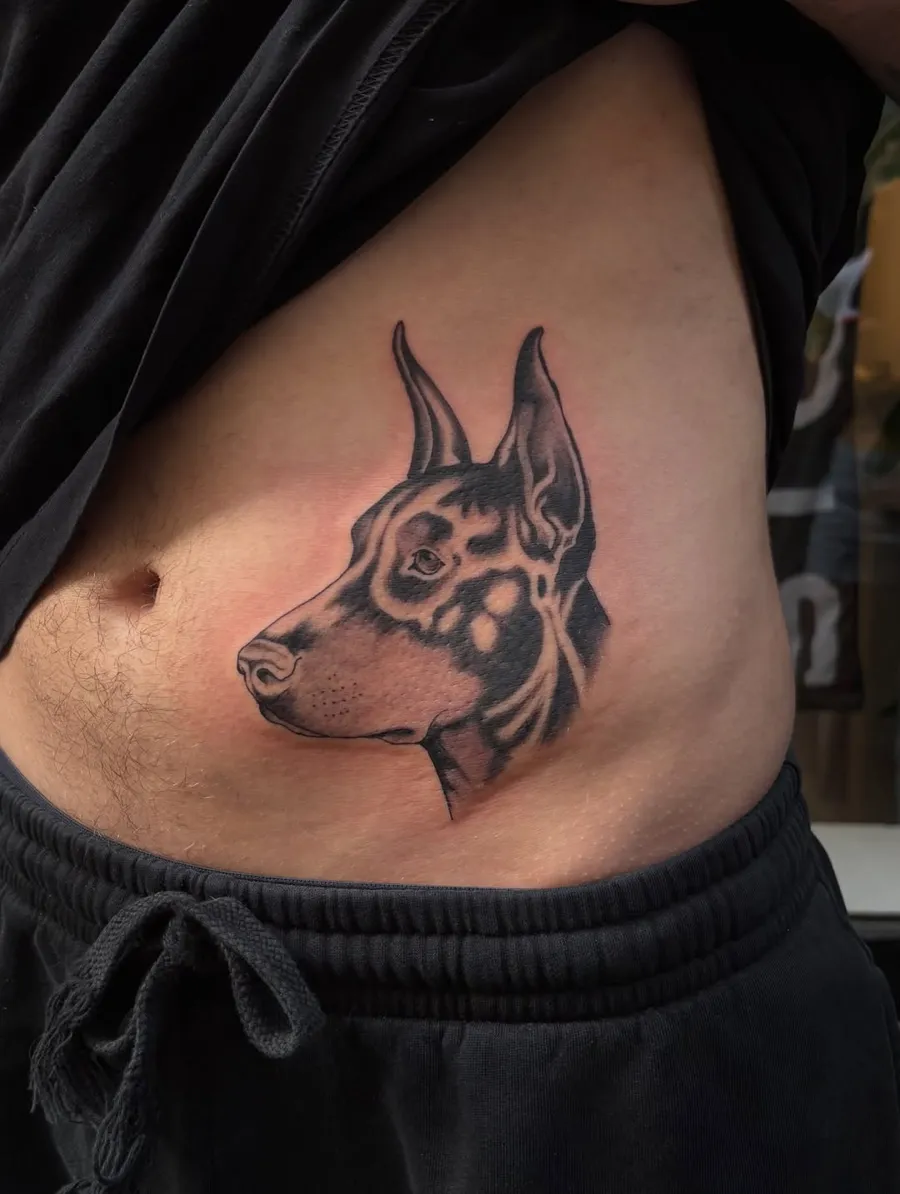 Tatouage de Lost Mustang : tête de doberman en noir et gris sur le flanc