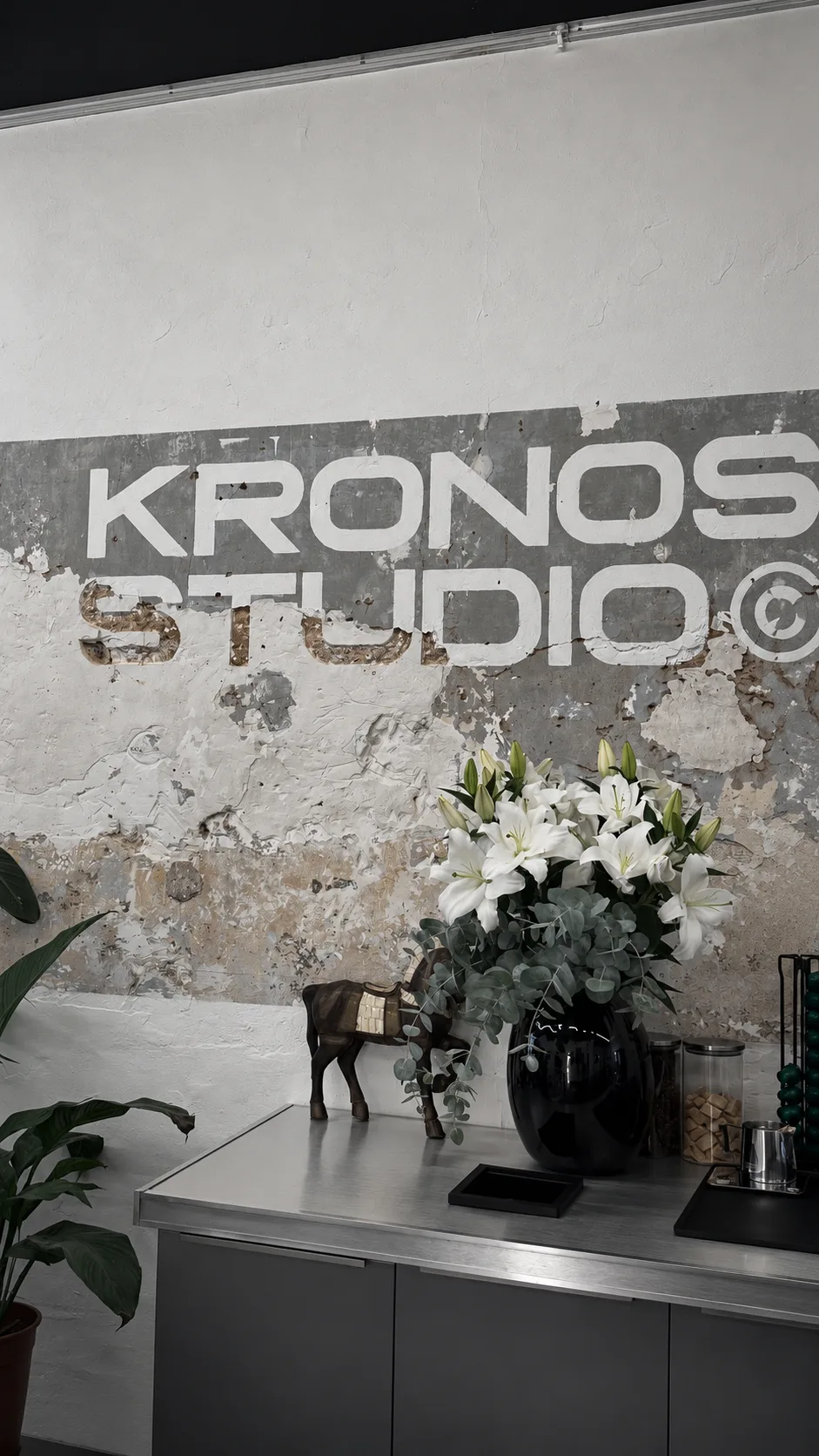 Le comptoir du studio : lys blancs, cheval en bois et lettrage Kronos Studio sur le mur en plâtre brut