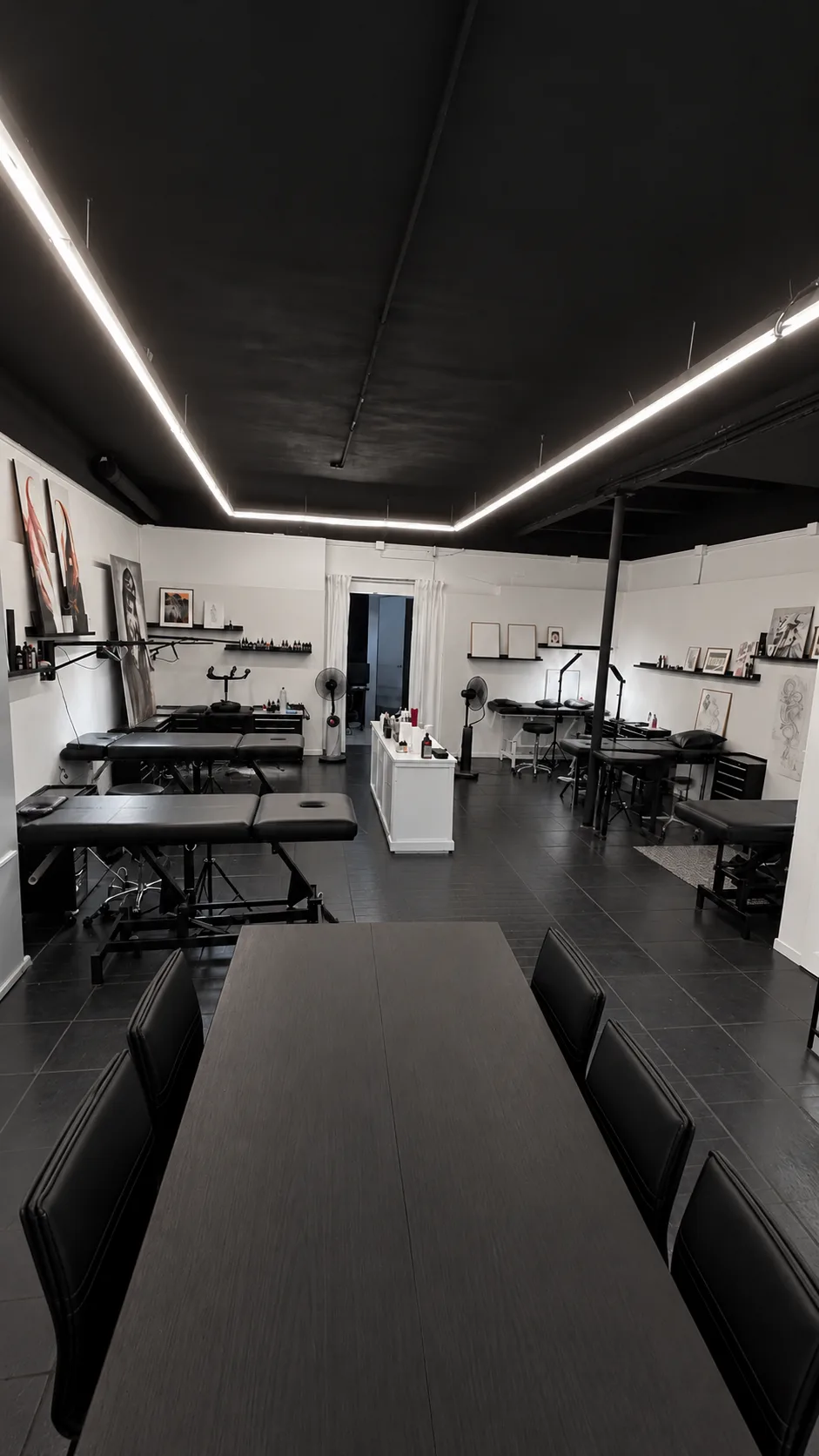 L'espace de tatouage : tables de soin noires, étagères d'encres et dessins aux murs, bandeau lumineux au plafond, grande table au premier plan