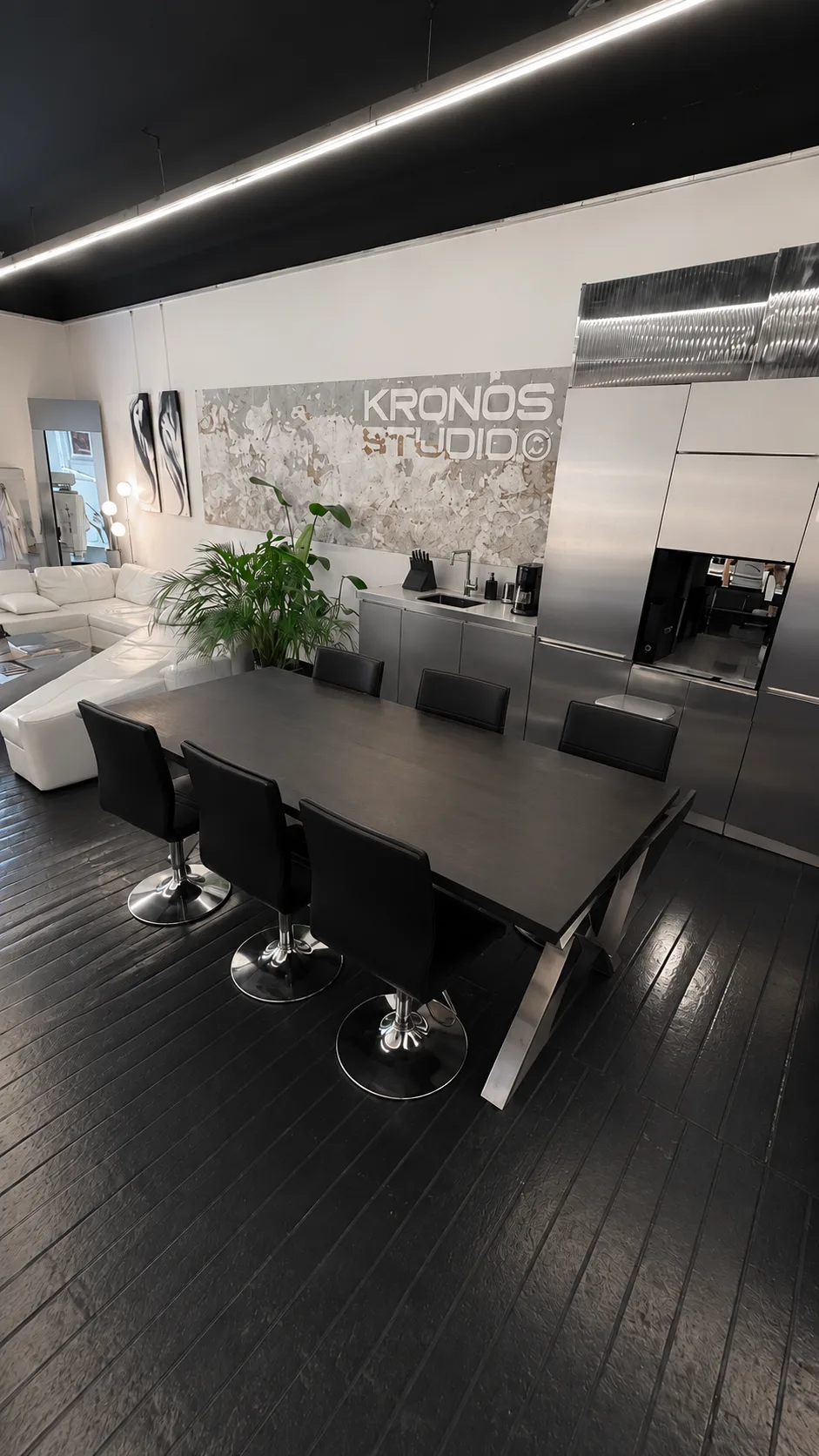 Le salon de tatouage Kronos Studio à Marseille : grande table noire, cuisine en inox, canapé blanc et lettrage Kronos Studio au mur